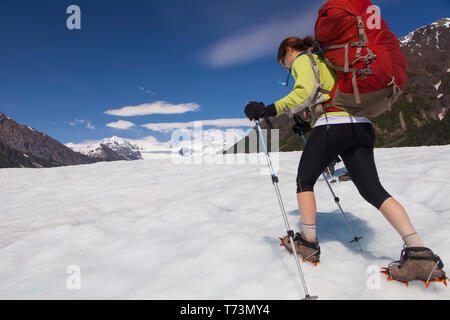 Donna backpacking attraverso il Root Glacier con ramponi durante l'estate verso Donoho Peak, Wrangell Mountains, Wrangell-St Parco Nazionale Elias,... Foto Stock