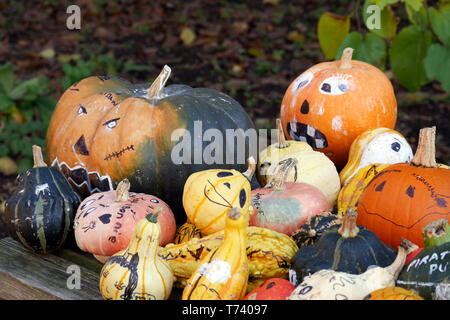 Un assortimento di zucche autunnali, zucche e zucche, con varie facce dipinte. Foto Stock