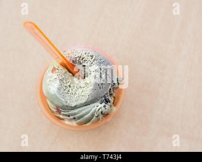 Una dose di gelato, sapore di pistacchio, in un contenitore di plastica di colore arancione. Nella parte superiore vi è un cucchiaio di plastica nello stesso colore all'interno. In vista superiore con p Foto Stock