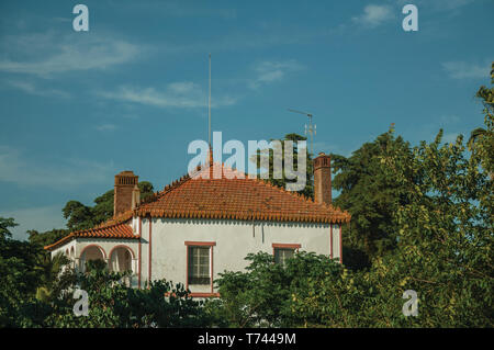 Tetto del cottage affascinante tra lussureggianti alberi verdi sul tramonto in un piccolo agriturismo vicino a Elvas. Una graziosa città sulla frontiera più orientale del Portogallo. Foto Stock