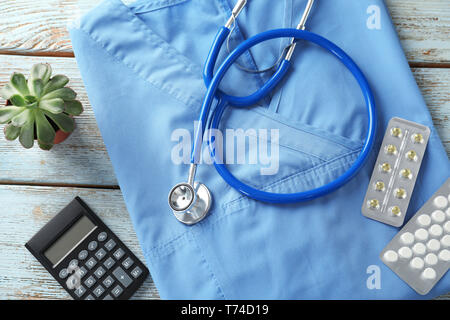 Composizione con medico uniforme e calcolatrice su sfondo di legno. Health care concept Foto Stock