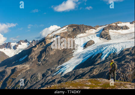 Un uomo a piedi vicino al Harding Icefield Trail con i monti Kenai e un ghiacciaio senza nome sospeso in background, Kenai Fjords National Park,... Foto Stock