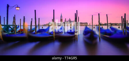 Gondole ormeggiate lungo la riva del Canal Grande durante una vibrante al tramonto con una vista di San Giorgio Maggiore e la chiesa della distanza Foto Stock