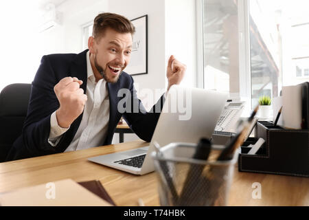 Felice imprenditore entusiasta con il computer portatile in ufficio Foto Stock