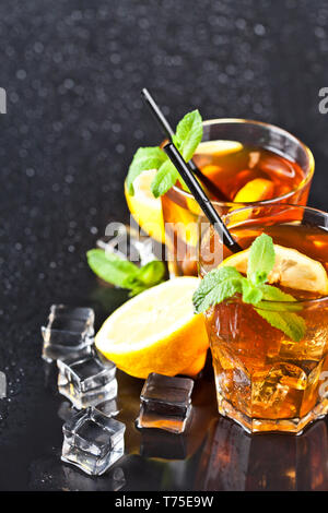 Due bicchieri con freddo tradizionale di tè freddo al limone e foglie di menta e i cubetti di ghiaccio umido su sfondo nero. Foto Stock