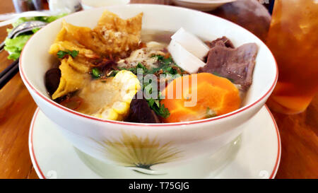 Delizioso Cibo vegetariano mais tofu carota fungo funghi Riso tagliatelle primavera zuppa di cipolla croccante di carta di riso in bianco ciotola tavolo in legno tè al limone ghiaccio Foto Stock