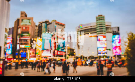 Blur scena della folla di persone in attesa al bivio occupato nella parte anteriore di Ximending al quartiere per lo shopping in Taipei durante il Blu Crepuscolo ora per attraversare il bivio Foto Stock