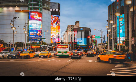 La sfocatura in movimento di incrocio occupato nella parte anteriore di Ximending al quartiere per lo shopping in Taipei durante il Blu Crepuscolo ora con taxi passando attraverso. Foto Stock