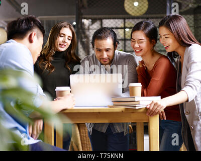 Un team di asiatici e caucasici gli imprenditori che lavorano insieme in ufficio utilizzando il computer portatile. Foto Stock