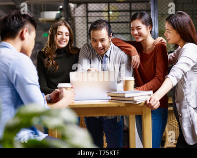 Gruppo di felice giovani imprenditori asiatici e caucasici e uomo donna riunione in ufficio discutere di affari con computer portatile. Foto Stock