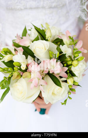 Bianco boccioli di rosa in combinazione con un grigio fresia e un rametto di gypsophila in bouquet della sposa su uno sfondo sfocato di un abito da sposa. Foto Stock