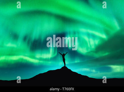 Aurora boreale e silhouette di donna con sollevata bracci sul picco di montagna. Isole Lofoten in Norvegia. Aurora e felice ragazza. Cielo stellato e pol Foto Stock