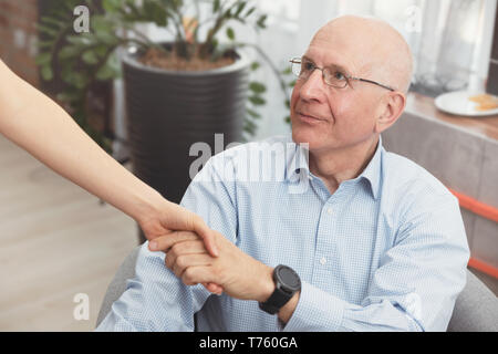 Salute e visitatori un anziano uomo durante la visita iniziale. Felice paziente trattiene il caregiver ad una mano mentre spendere tempo insieme Foto Stock