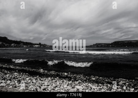 Le onde in arrivo al Gnejna Bay di Malta. Un paesaggio marino di Malta durante la primavera di Gnejna Bay in bianco e nero. Foto Stock