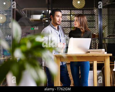 Asian business man e caucasico business donna avente una discussione in ufficio utilizzando il computer portatile. Foto Stock