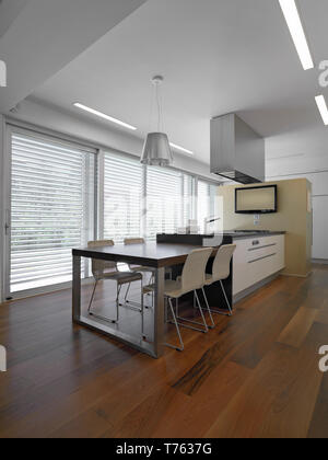 Scatti di interni di una cucina moderna con cucina isalnd il pavimento è di legno in primo piano il tavolo da pranzo in legno Foto Stock
