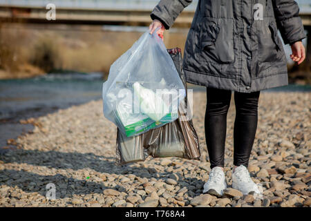 Garbage in natura, la pulizia dell'ambiente in primavera sul fiume dalle macerie di una donna in lattice monouso guanti blu nel grande blu Foto Stock