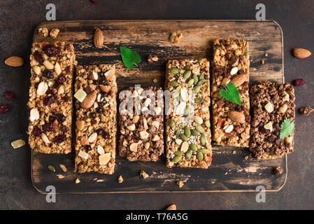 Varie granola bar su scuro dello sfondo rustico, vista dall'alto. In casa snack sano muesli - super bar. Foto Stock