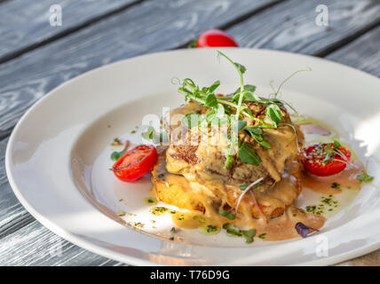 Bistecca di manzo su golden croccanti di patate con formaggio e pomodori, guarnita con microgreen sul tavolo in una giornata di sole Foto Stock