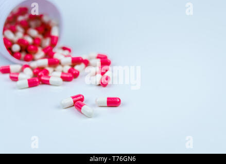 Rosa e Bianco capsule pillola versato fuori dalla bottiglia di plastica bianca contenitore. Global Healthcare concetto. Antibiotici la resistenza al farmaco. Agenti antimicrobici Foto Stock
