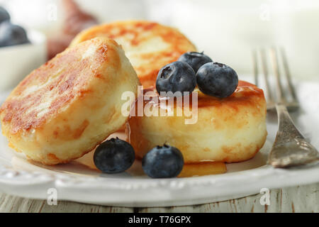 Cottage cheese pancakes, syrniki, frittelle di cagliata con frutti di bosco freschi mirtillo e miele in una piastra bianca. Colazione Gourmet. Messa a fuoco selettiva Foto Stock