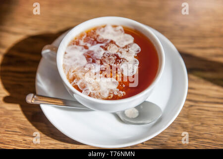 Primo piano di un tavolo di legno con una tazzina bianca e appena versata la crema di diffondere in una forma poco nuvoloso. Questa forma di preparazione del tè è diventato una tradizione. Foto Stock