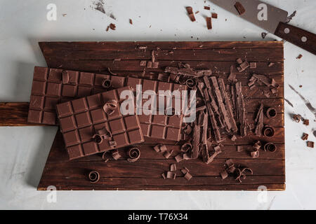 Tagliere in legno con pezzi di cioccolato su sfondo chiaro Foto Stock