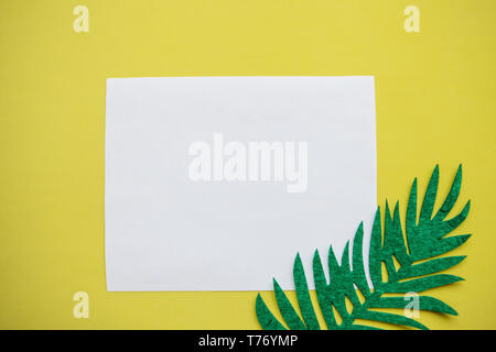 Foglio di carta bianca per il testo e a fianco di un foglio di feltro di felce su sfondo giallo. Estate design in stile minimal. Foto Stock