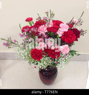 Bouquet di fiori con rose rosse in un vaso su una scrivania Foto Stock