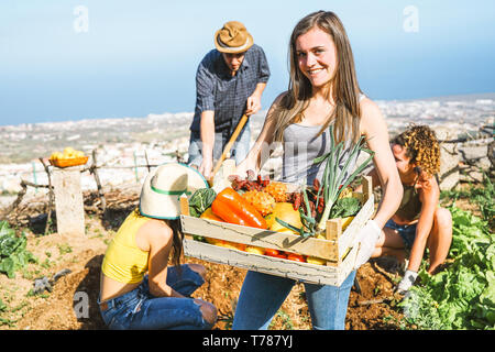 Gruppo di amici che lavorano insieme in una farm house - Happy giovane donna azienda cassetta da frutta con verdure fresche in casa del giardino Foto Stock