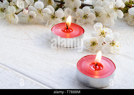 Candele di cera stanno bruciando vicino i rami della fioritura ciliegia sulla tabella. Close-up. Foto Stock