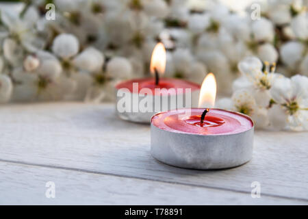 Primo piano della candele rosse vicino a rami di bianco fiori di ciliegio. Candela che brucia Foto Stock