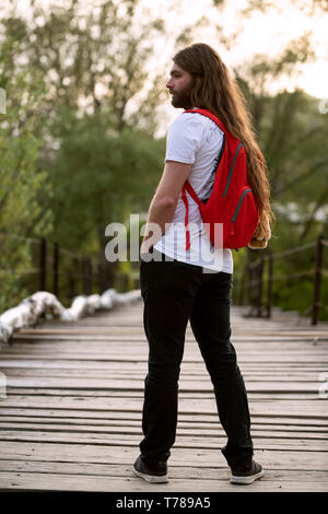 Maschio con tshirt e backback è in piedi su un ponte di legno in primavera Foto Stock