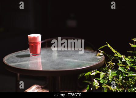 Bevanda alla moda, bacca rossa caffè latte con schiuma sulla tabella trasparente in street cafe. Foto Stock