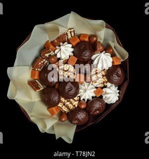 Marshmallows nel cioccolato, caramelle cioccolata e altri deliziosi dolci, imballati come un bouquet, stando in piedi in un vaso di vetro su uno sfondo nero. A Foto Stock