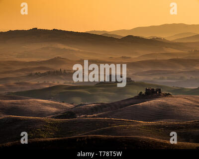 Sunrise toscano rispetto alle aziende nella campagna collinare della Toscana, Italia Foto Stock