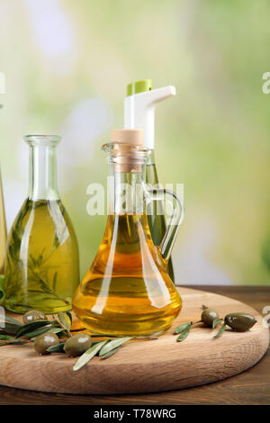 Vetreria con olio di oliva sulla tavola di legno contro sfondo sfocato Foto Stock