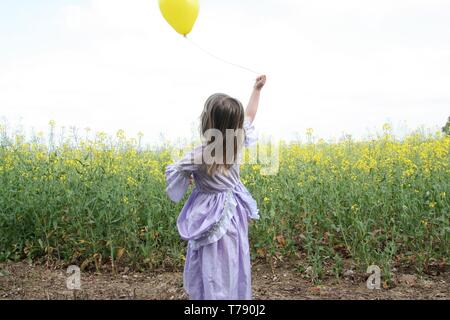 Ragazza in abito viola holding palloncino giallo Foto Stock
