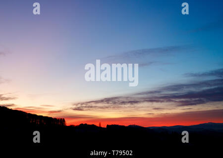 Tramonto colorato con incandescente nuvole e un albero di una collina e valle silhouette nelle Alpi austriache Foto Stock