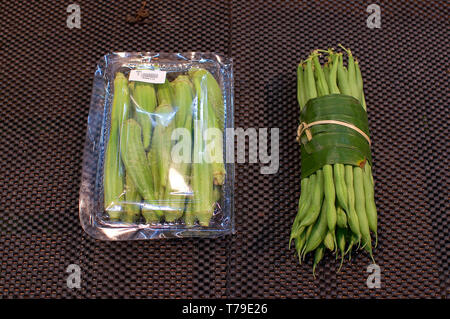 L'Okra raggruppati in una confezione di plastica e fagioli avvolti in foglie di banana tenuto in mani femminili. Questa è una soluzione eccellente come sostituire la confezione di plastica una Foto Stock