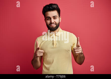 Awesome positivo uomo barbuto in elegante giallo T-shirt indica felicemente alla telecamera. close up foto. isolato sfondo rosa Foto Stock