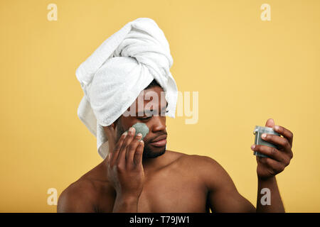 Ragazzo afro usando la crema dopo aver fatto la doccia isolate su sfondo giallo, studio shot.cosmetologia, concetti cosmetici. Foto Stock