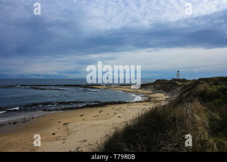 Vista su una baia con una spiaggia di sabbia e il cielo nuvoloso, bianco faro nel retro, Isola del Sud, Nuova Zelanda Foto Stock