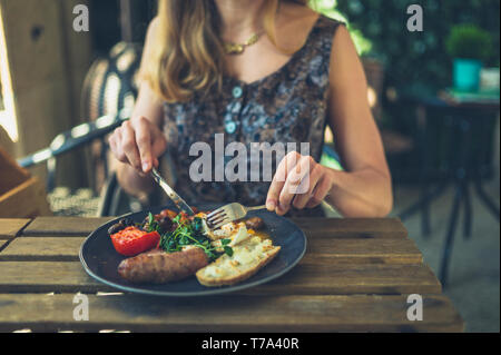 Una giovane donna è avere la prima colazione con la salsiccia in un ristorante all'aperto Foto Stock