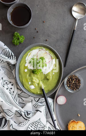 Close up gustosa minestra in crema di broccoli e crema e ravanelli in una terrina il pane e il cucchiaio a sfondo grigio, bianco igienico vicino su sfondo di calcestruzzo. Co Foto Stock