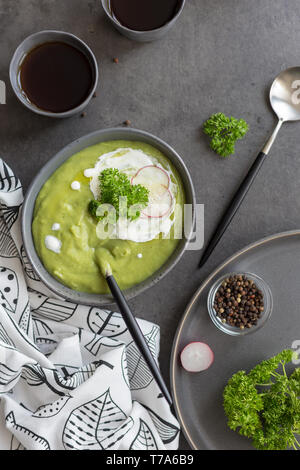 Una sana minestra in crema di broccoli e panna acida, cucchiaio, pepe e igienico vicino sul cemento grigio. Concetto di dieta alimentare estiva. Vista superiore, fla Foto Stock