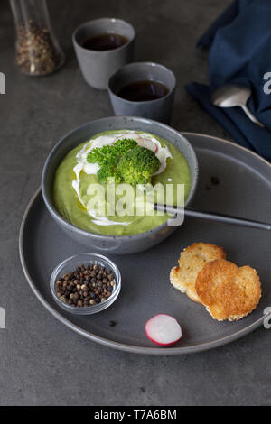 Una sana minestra in crema di broccoli e panna acida con radicchio, cucchiaio, pepe e igienico vicino sul cemento grigio. Concetto di dieta alimentare estiva. s Foto Stock