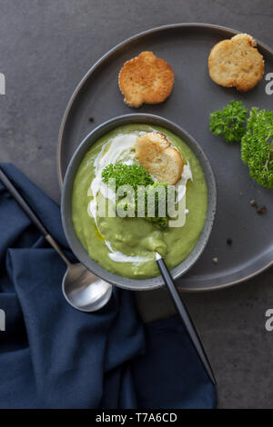 Una sana minestra in crema di broccoli e panna acida, cucchiaio, toast, pepe e igienico vicino sul cemento grigio. Concetto di dieta alimentare estiva. Top v Foto Stock