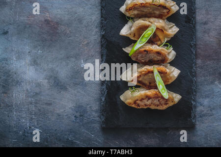 Giapponese gnocchi gyoza sulla pietra nera piastra, copia dello spazio. Foto Stock