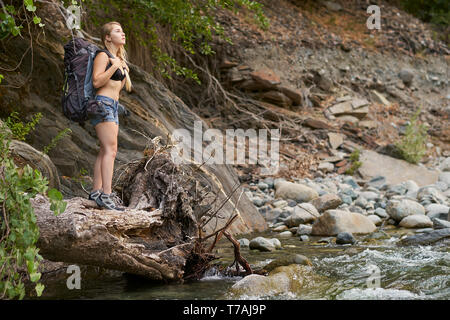 Un avventuroso giovane donna escursionismo fino a creek con uno zaino su un assolo di backpacking viaggio da solo nella foresta e sulle montagne Foto Stock